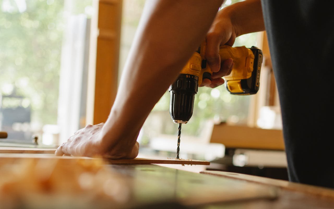 About Crop anonymous male drilling timber plank with professional screwdriver on table in workshop