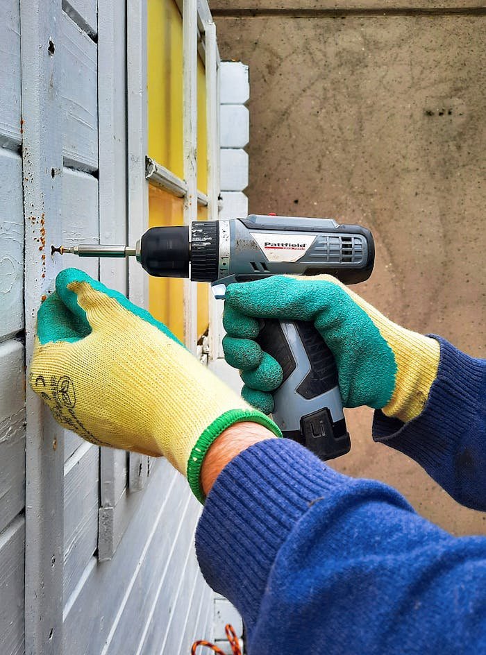 About Close-up of a construction worker using a drill on a wooden wall, focusing on hands and tool.